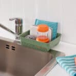 Green kitchen drain organizer with cleaning supplies and kitchen towels for efficient organization.