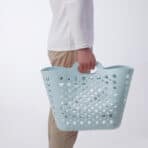 Light blue perforated plastic shopping basket held by a person in casual attire.
