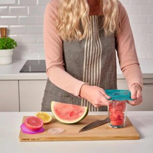 Watermelon being cut in a kitchen, using a storage container for fresh fruit, under bright indoor lighting.
