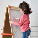 Child drawing on magnetic whiteboard with colorful markers.