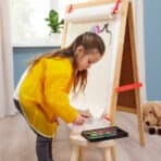 Bright kid engaging in watercolor painting with art supplies and easel.