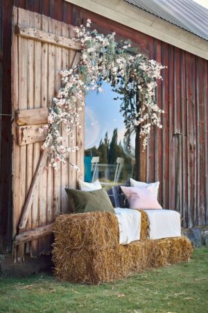 Beautiful rustic outdoor seating with hay bales, cushions, and floral arch on barn wall.