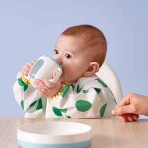 Baby drinking from a white and blue mug, sitting at a table.