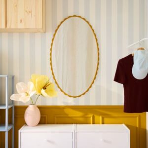 Oval dark yellow mirror hanging on striped wall with decor items.