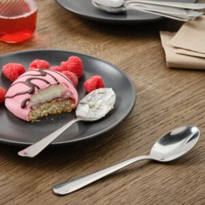 Stainless steel dessert spoon on table with cake and raspberries.