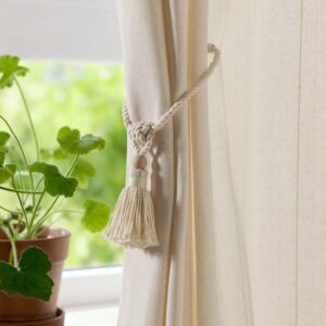 Off-white magnetic curtain tie-back with tassel for elegant window decor.