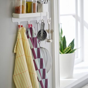 Kitchen hooks holding colorful towels and utensils near a window.